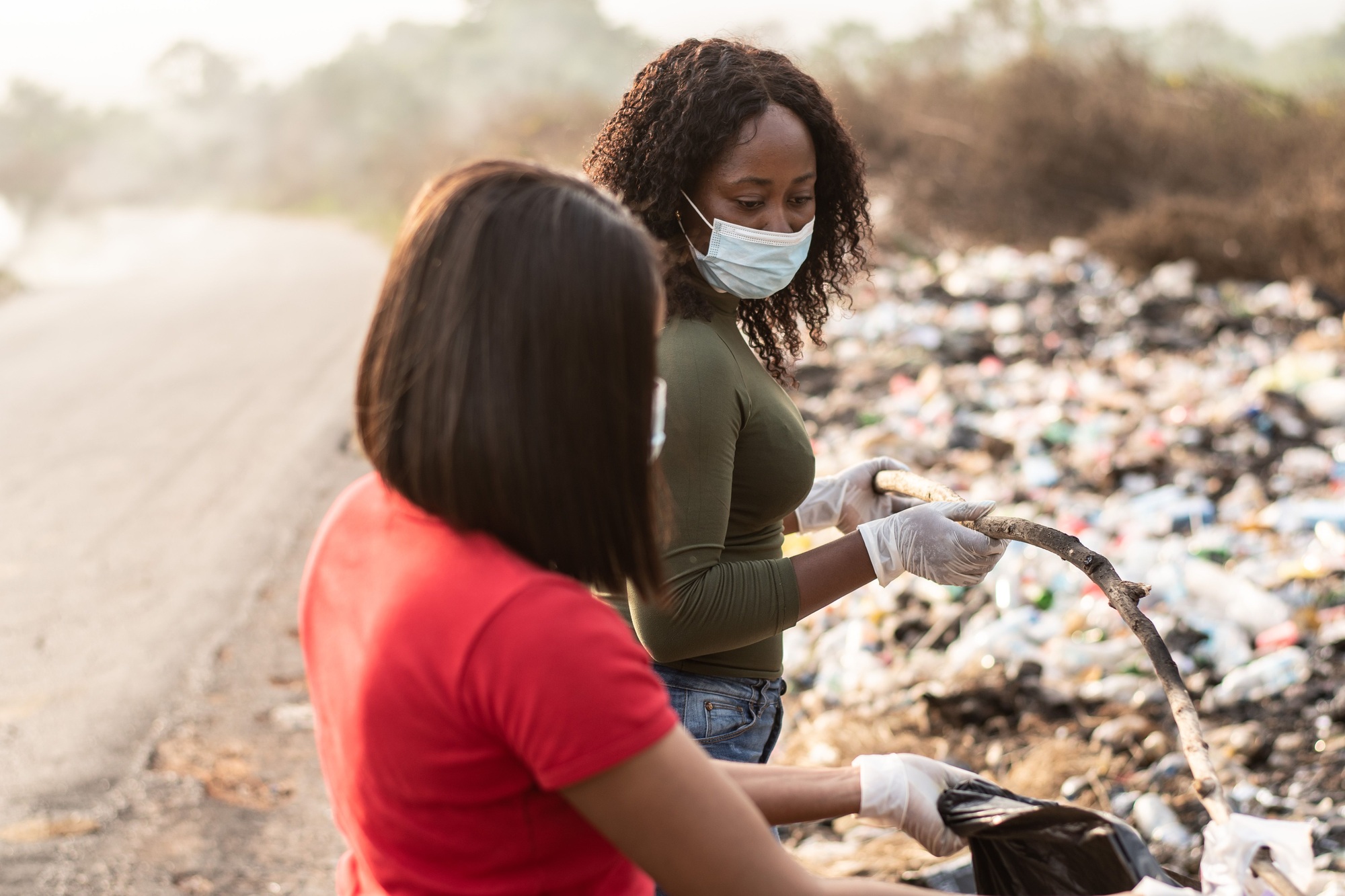 Nigerian women cleaning up together a dump site with a road in the background in Nigeria